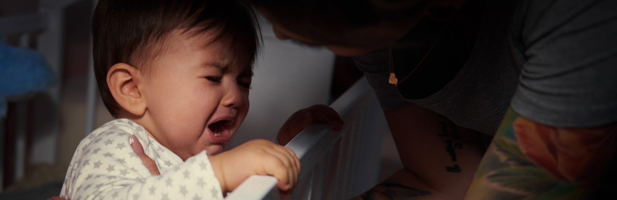 baby crying holding on to the rail of a cot