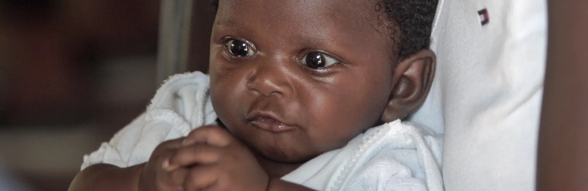 dark skinned baby in white clothes wide awake