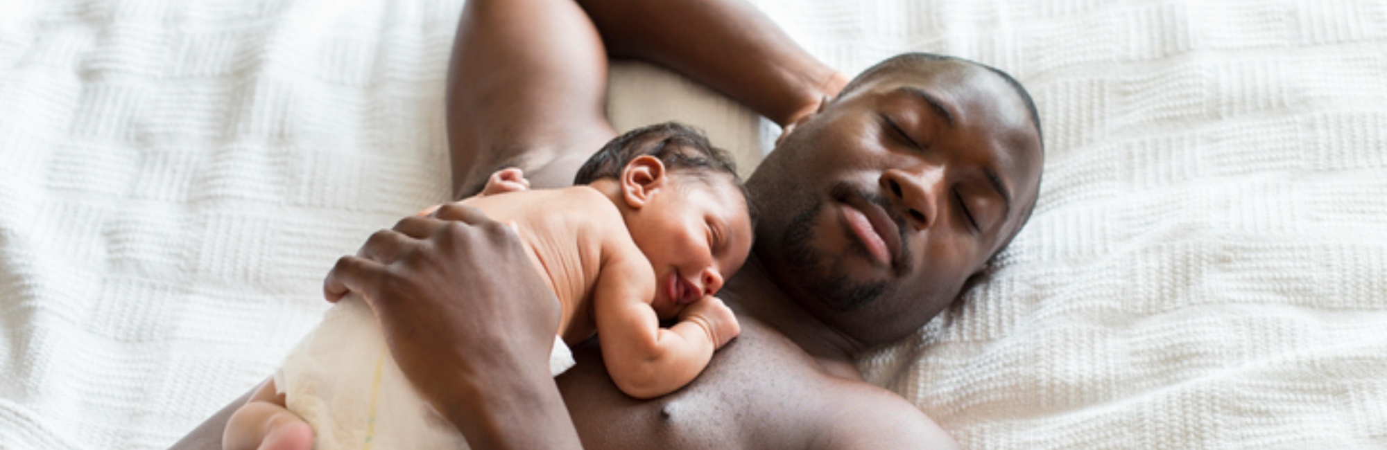 a shirtless father and baby nap together on a safe surface