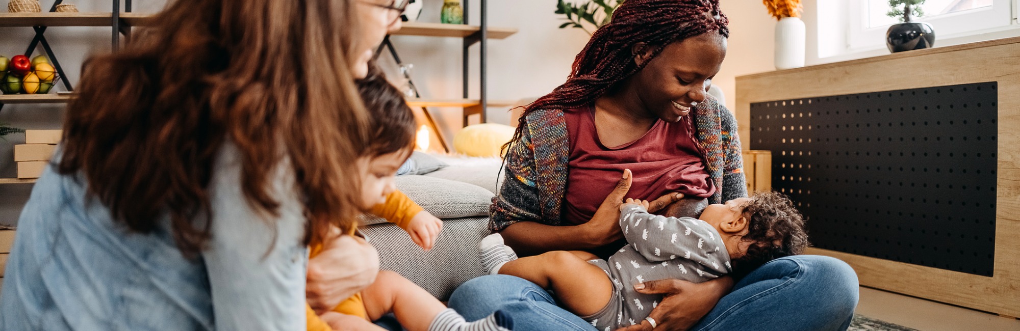 mother breastfeeds her baby while other mother plays with baby in lap