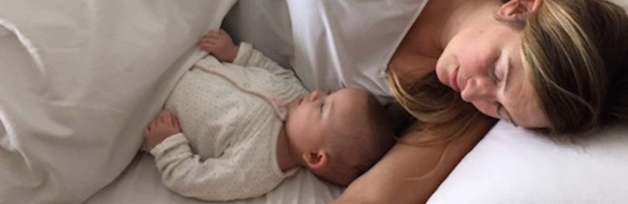 mother sleeps on her side in bed with baby who is sleeping on its back close to her